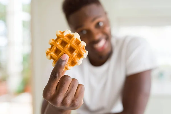 African american man eating sweet Belgian waffle with a happy face standing and smiling with a confident smile showing teeth