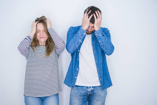 Young beautiful couple standing together over white isolated background suffering from headache desperate and stressed because pain and migraine. Hands on head.