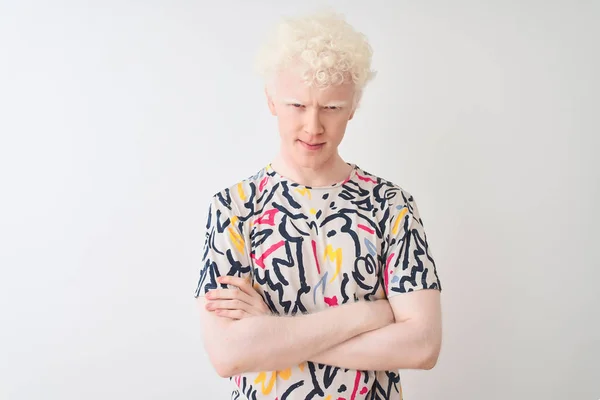 Young albino blond man wearing colorful t-shirt standing over isolated white background skeptic and nervous, disapproving expression on face with crossed arms. Negative person.