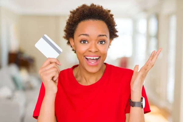 Young african american woman holding credit card very happy and excited, winner expression celebrating victory screaming with big smile and raised hands