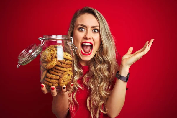 Jovem Bela Mulher Segurando Frasco Biscoitos Sobre Fundo Vermelho Isolado — Fotografia de Stock