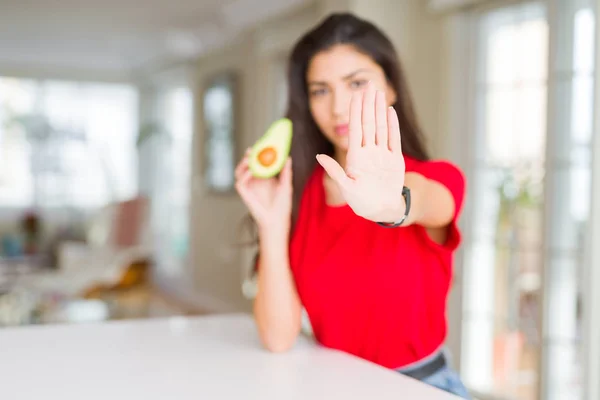 真剣で自信に満ちた表情でストップサインを行うオープンハンドで健康的なアボカドを食べる若い女性 防衛ジェスチャー — ストック写真