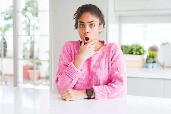 Beautiful african american woman with afro hair wearing casual pink sweater Looking fascinated with disbelief, surprise and amazed expression with hands on chin