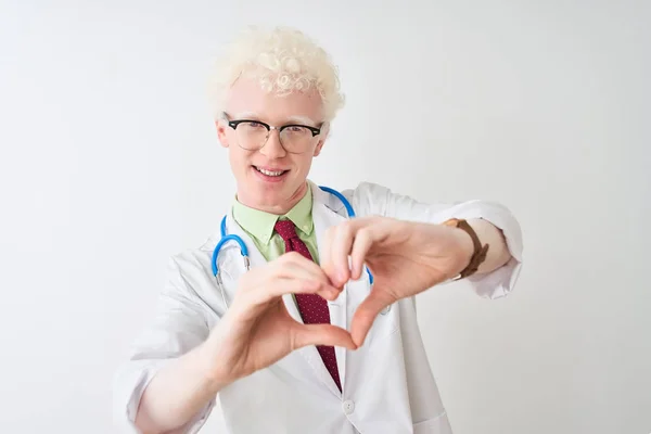 手でハートのシンボルと形を示す愛に笑みを浮かべて孤立した白い背景の上に立って聴診器を身に着けている若いアルビノの医師の男 ロマン主義 — ストック写真