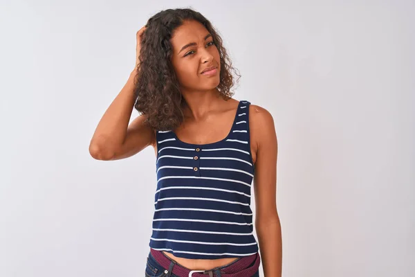 Young brazilian woman wearing striped t-shirt standing over isolated white background confuse and wonder about question. Uncertain with doubt, thinking with hand on head. Pensive concept.