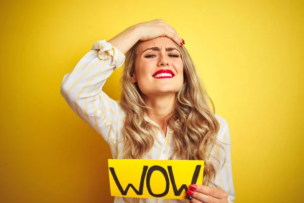 Beautiful woman holding amazed wow surprise banner over isolated yellow background stressed with hand on head, shocked with shame and surprise face, angry and frustrated. Fear and upset for mistake.