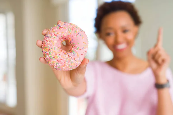 若いアフリカ系アメリカ人女性ピンクシュガードーナツを食べる幸せな顔をしたアイデアや質問指差し指で驚いて ナンバーワン — ストック写真