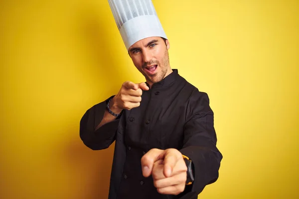 年轻厨师 身穿制服 头戴帽子 站在孤立的黄色背景上 手指指向镜头 脸上洋溢着欢乐滑稽的表情 好的能量和活力 — 图库照片