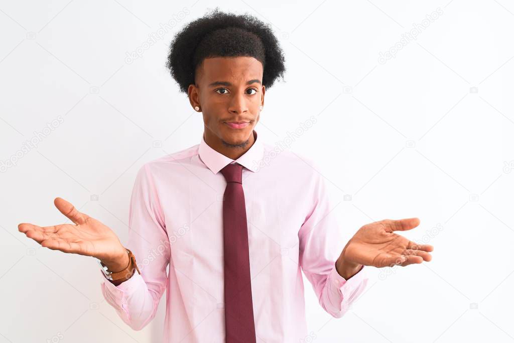 Young african american businessman wearing tie standing over isolated white background clueless and confused expression with arms and hands raised. Doubt concept.