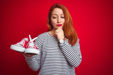 Güzel, kızıl saçlı, spor ayakkabılarını kırmızı arka planda tutan genç bir kadın. Ciddi bir yüz. Soru sormayı düşünüyor, kafası karışık bir fikir.