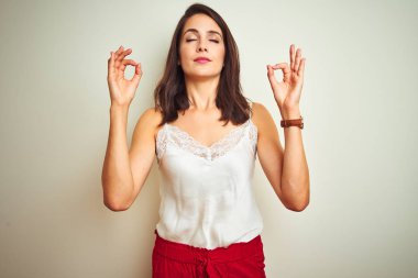 Beyaz izole arka plan üzerinde duran t-shirt giyen genç güzel kadın dinlenmek ve parmakları ile meditasyon jest yapıyor kapalı gözleri ile gülümseyerek. Yoga konsepti.