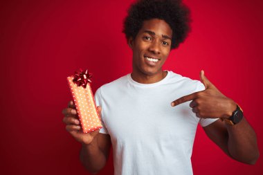 Sevgililer günü hediyesini elinde tutan Afro-Amerikalı genç adam izole edilmiş kırmızı arka planda durup kendini işaret ediyor.