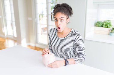 Genç Afrikalı Amerikalı kadın yatırım olarak kumbara içine bozuk para koyuyor ya da sürpriz bir yüzle korku dolu ve korku ifadesinden heyecanlanmış bir şekilde şoktan kurtarıyor.