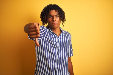 Rasta desenli tişörtlü Afro bir adam izole edilmiş sarı arka plan üzerinde mutsuz, reddedilmiş ve olumsuz jest yapmış görünüyor. Kötü ifade.
