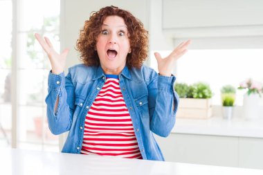 Orta yaşlı, kıvırcık saçlı, kot ceketli, çılgın bir kutlama yapan ve kolları havada, gözleri açık, heyecanlı bir şekilde bağıran bir kadın. Kazanan konsept