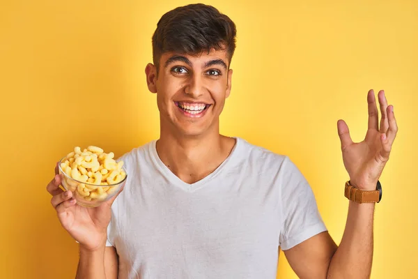 Jovem Indiana Segurando Tigela Com Milho Extrudado Sobre Fundo Amarelo — Fotografia de Stock