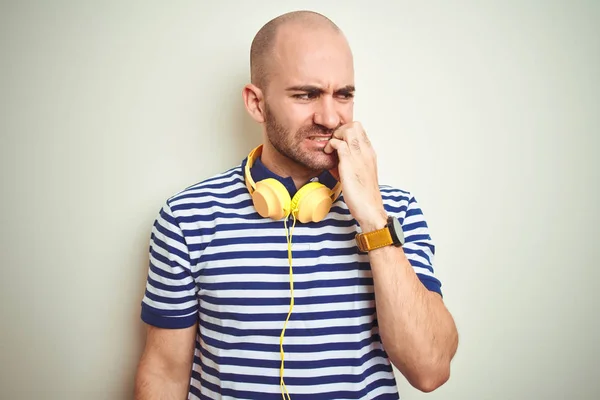 Young man listening to music wearing yellow headphones over isolated background looking stressed and nervous with hands on mouth biting nails. Anxiety problem.