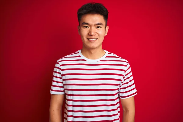 縞模様のTシャツを着た若いアジア系中国人男性が 幸せとクールな笑顔で孤立した赤い背景の上に立っています 運のいい人 — ストック写真