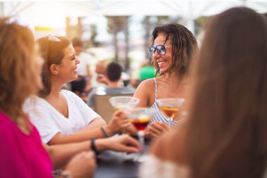 Güzel bir grup kadın restoranın terasında oturmuş kokteyller içiyor konuşuyor ve gülümsüyor.