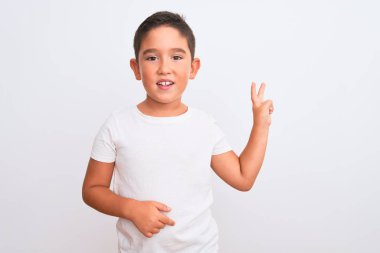 Güzel çocuk, izole edilmiş beyaz arka plan üzerinde sıradan bir tişört giyip kameraya bakıp gülümsüyor ve zafer işareti yapıyor. İki numara..
