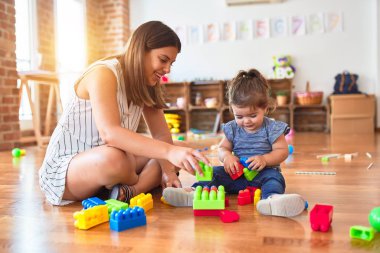 Genç, güzel öğretmen ve bebek anaokulunda yapı taşı oyuncaklarıyla oynuyorlar.