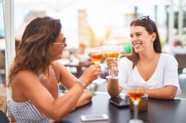 Güzel anne ve kızı restoranın terasında oturmuş kokteyl içiyor ve gülümsüyor.