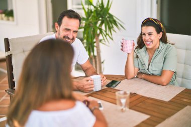 Güzel bir aile terasta oturmuş kahve içiyor, konuşuyor ve gülümsüyor.
