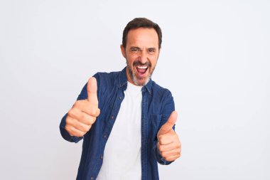 Mavi kot gömlek giyen orta yaşlı yakışıklı adam izole edilmiş beyaz arka plan üzerinde duruyor. Elle olumlu jest yapıyor, gülümsüyor ve başarı için mutlu. Kazanan jest.