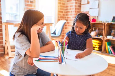Güzel öğretmen ve küçük kız anaokulunda renkli kalemlerle resim çiziyor.