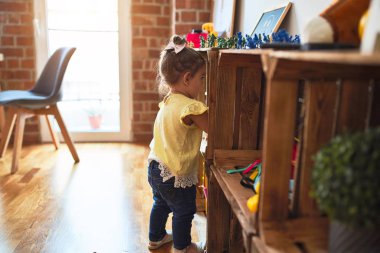 Güzel çocuk anaokulunda oyuncaklarını rafa kaldırıyor.