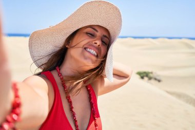 Güneş banyosu giyen genç ve güzel bir kadın Maspalomas Dunes bech 'te akıllı telefon kullanarak selfie çekiyor.