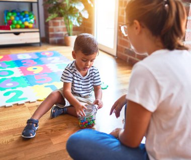 Güzel öğretmen ve küçük çocuk anaokulunda oturmuş küçük çikolata toplarını yiyorlar.
