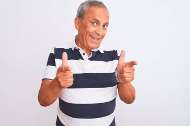 İzole edilmiş beyaz arka planda dikilen, sıradan çizgili polo giyen yaşlı gri saçlı adam mutlu ve komik yüzlü parmaklarını kameraya doğrultuyor. İyi enerji ve titreşimler.