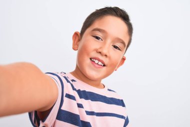 Sıradan çizgili tişört giyen güzel bir çocuk izole edilmiş beyaz arka planda selfie çekiyor. Mutlu bir yüzü var ve kendine güvenen bir gülümsemeyle dişlerini gösteriyor.