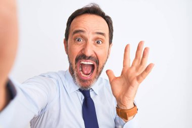 Orta yaşlı iş adamı kravat takıyor ve selfie çekiyor. İzole edilmiş beyaz arka planda mutlu ve heyecanlı duruyor. Kazanan ifade zaferi kutluyor.