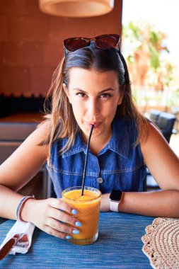 Genç ve güzel bir kadın restoranda oturmuş yaz tatilinin tadını çıkarıyor sağlıklı meyve suyu içiyor.