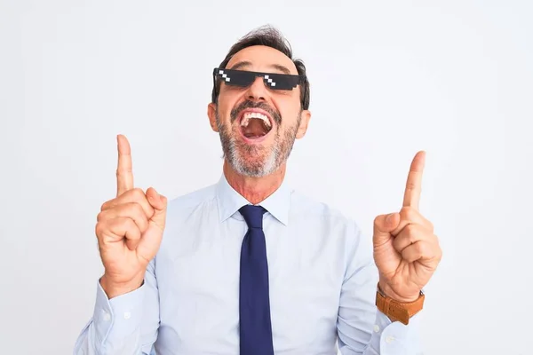 Middle age businessman wearing thug life sunglasses over isolated white background amazed and surprised looking up and pointing with fingers and raised arms.