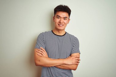 Çizgili tişört giyen Asyalı genç bir adam izole edilmiş beyaz arka planda duruyor ve kollarını kavuşturup kameraya bakıyor. Pozitif kişi.