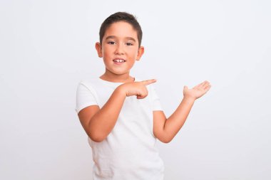 İzole edilmiş beyaz arka plan üzerinde duran sıradan tişört giyen güzel çocuk kameraya hayret ediyor ve gülümsüyor..