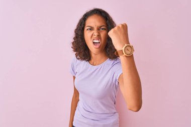 İzole edilmiş pembe arka plan üzerinde duran Brezilyalı genç bir kadın öfkeyle bağırırken kızgın ve öfkeli bir şekilde yumruğunu kaldırıyor. Öfke ve agresif kavram.