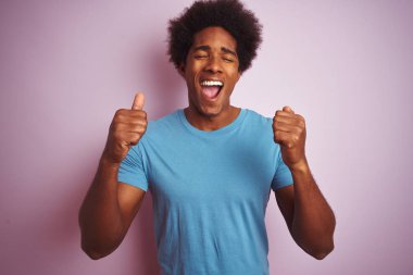 Afro saçlı, mavi tişörtlü bir Afro-Amerikalı başarılı olmak için heyecanlı, kolları havada ve gözleri kapalı zafer tebessümü ile izole edilmiş pembe arka plan üzerinde duruyor. Kazanan konsept.