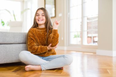 Evde oturan güzel genç kız çocuk mutlu yüz zafer işareti yapıyor kamera göz kırpıyor ile gülümsüyor. İki numara.