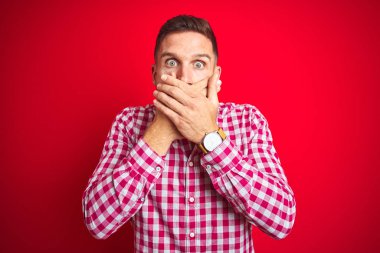 Kırmızı izole edilmiş arka plan üzerinde genç yakışıklı bir adam ağzını yanlışlıkla ellerinle kapatarak şok etti. Gizli konsept.