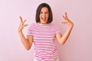 İzole edilmiş pembe arka planda duran çizgili tişört giyen genç ve güzel bir kadın başarı için deli ve çılgınlığı kutluyor kollarını kaldırmış ve gözleri kapalı heyecanla bağırıyor. Kazanan konsept