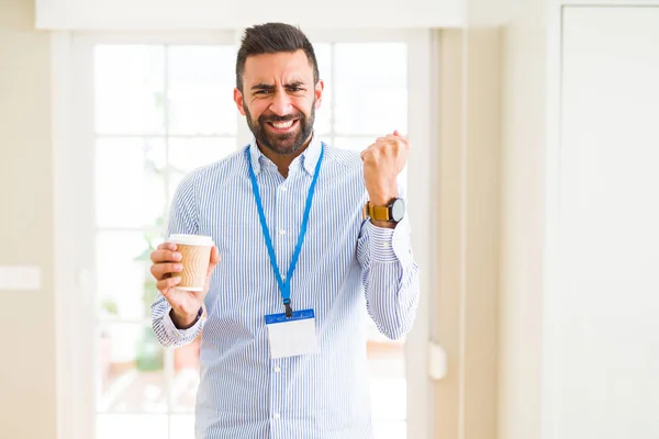 Handsome hispanic man wearing id card and drinking a cup of coffee annoyed and frustrated shouting with anger, crazy and yelling with raised hand, anger concept