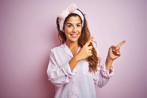 Young beautiful woman wearing pajama standing over pink isolated background smiling and looking at the camera pointing with two hands and fingers to the side.