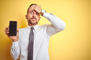 Genç yakışıklı iş adamı, sarı izole edilmiş arka planda akıllı telefon ekranı gösteriyor. Elleri başının üstünde, utanç ve şaşkınlık dolu, sinirli ve hayal kırıklığına uğramış bir halde. Hata için korku ve üzüntü.