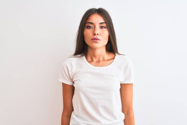 İzole edilmiş beyaz arka planda duran günlük tişört giyen genç ve güzel bir kadın yüzünde ciddi bir ifadeyle rahatlamış. Basit ve doğal bir şekilde kameraya bakıyorsun..