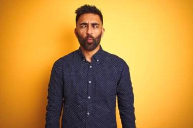 Genç ve yakışıklı Hintli işadamı, izole edilmiş sarı arka plan üzerine gömlek giyip dudaklarıyla balık suratı yapıyor, çılgınca ve komik hareketler yapıyor. Komik ifade.