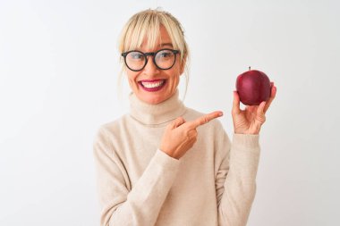 Elma tutan orta yaşlı bir kadın soyutlanmış beyaz arka planda duruyor. Elle ve parmakla işaret ederek çok mutlu.